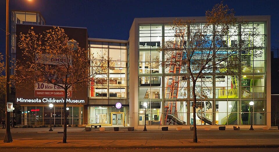 The Minnesota Children's Museum building illuminated at night in downtown Saint Paul, its lit windows reflecting on the surrounding sidewalk