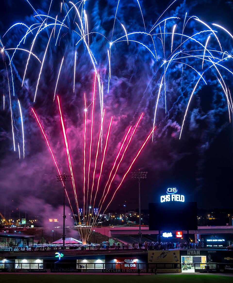 Bright fireworks bursting above CHS Field in Lowertown Saint Paul after a Saints game, lighting up the night sky over the ballpark and surrounding buildings