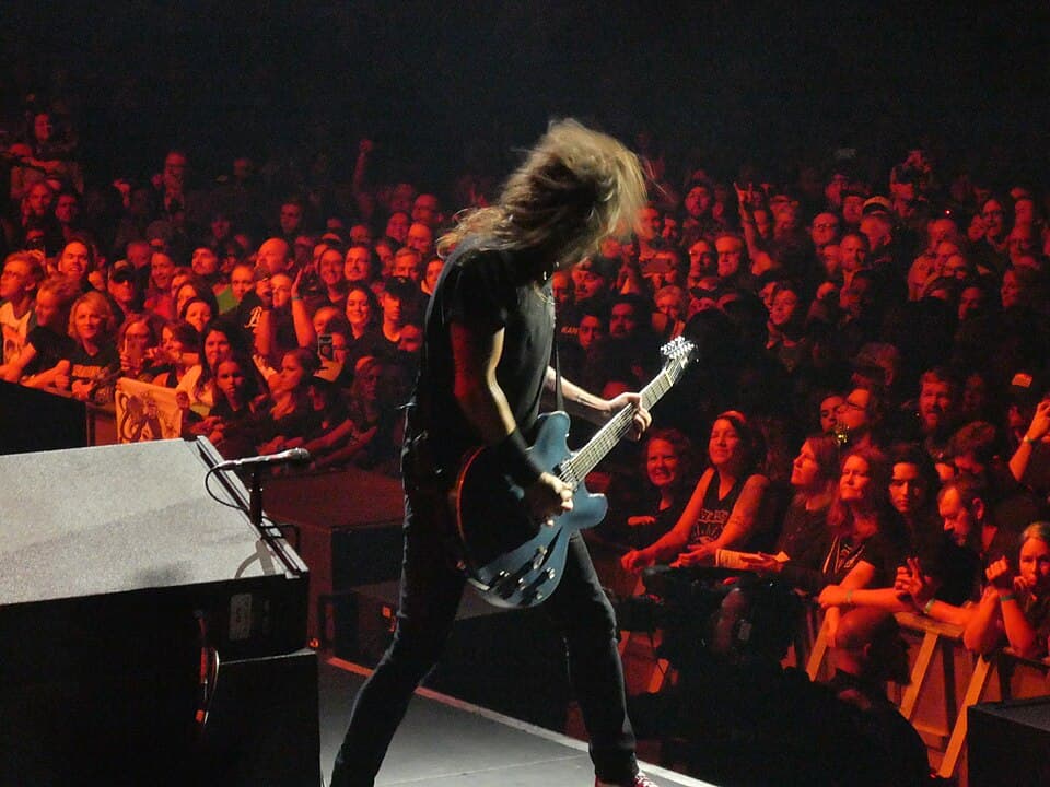 Foo Fighters performing on a brightly lit stage at Xcel Energy Center in Saint Paul, with a massive crowd filling the arena floor